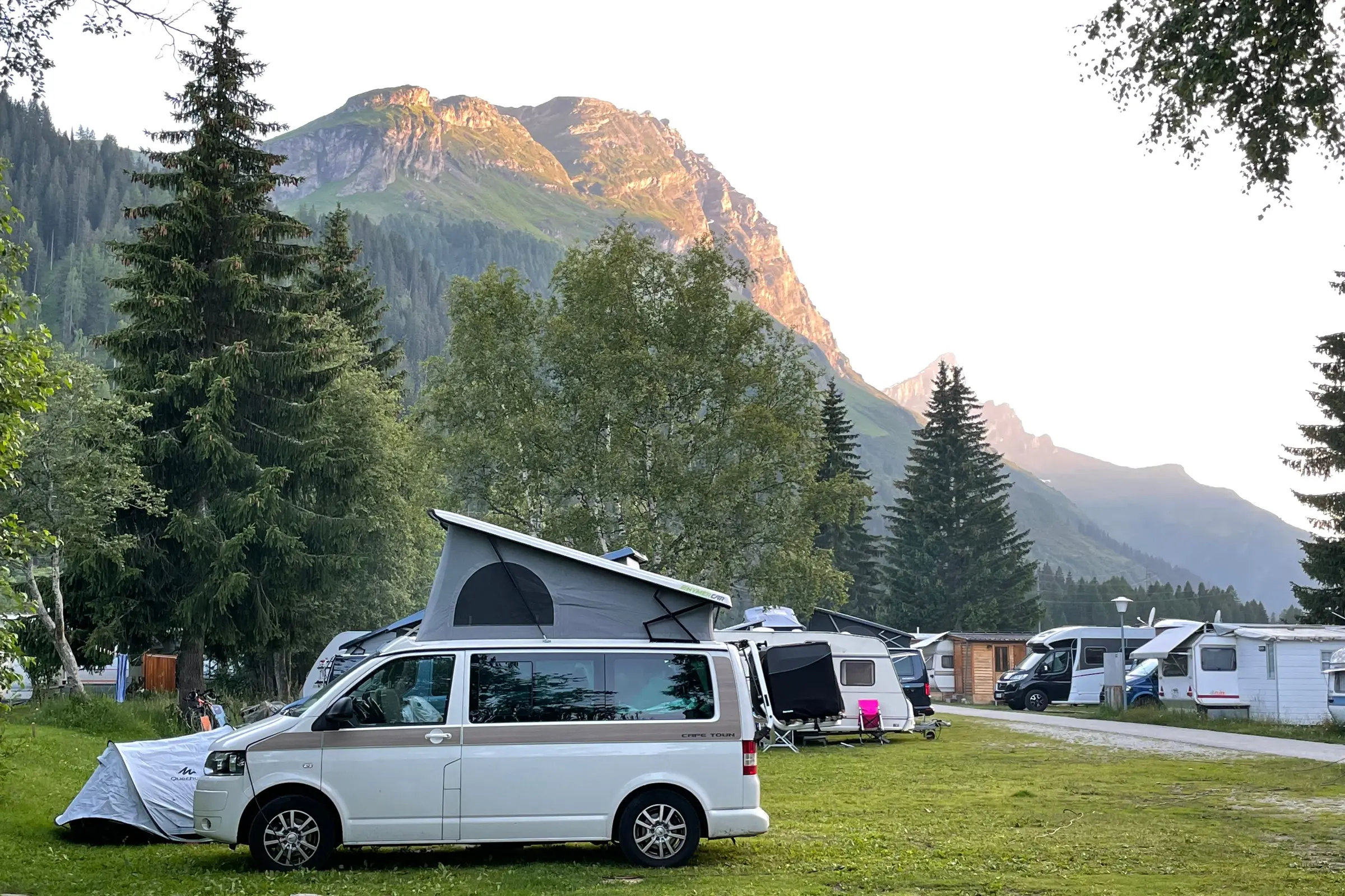 Camping en montagne au coucher du soleil, tentes et camping-cars sur l'herbe